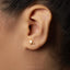 A close-up view of a person's ear, showing a small gold earring with a dragon design.