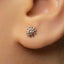 A close-up of a person's ear with a small silver earring featuring a sun-like design.