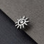 A silver-colored metal pin or bangle with a sun-like design is resting on a textured gray surface.