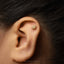 A gold earring with a sun-like design is visible in the ear of a person.