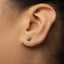 A close-up of a person's ear with a small silver earring featuring a sun-like design.