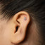 A close-up of a person's ear with a small silver letter 'S' piercing in the earlobe.