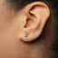 A close-up of a person's ear with a small silver earring featuring a small figure or character attached to it.