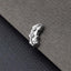 A small, silver-colored metal object, possibly a piece of jewelry, is resting on a textured gray surface.