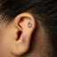A close-up of a person's ear with a small, silver earring in the earlobe.