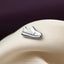A silver shoe pin is resting on a white fabric surface.