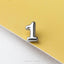 A shiny silver number one is placed on a yellow surface.
