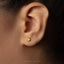 A close-up of a person's ear with a small gold earring featuring a hand sign.