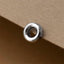 A silver-colored metal ring or bangle is resting on a textured surface, such as a piece of paper or cardboard.