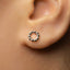 A close-up view of a person's ear with a small, round earring featuring a small, circular design in the center.