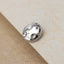A silver-colored metal object with a circular shape and small holes is resting on a textured surface.