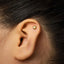 A close-up of a person's ear with a small gold earring in the earlobe.