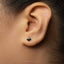 A close-up view of a person's ear with a small black earring featuring a spade symbol in the earlobe.