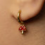 A close-up of a person's ear wearing a gold hoop earring with a red mushroom charm hanging from it.