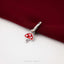 A silver mushroom charm with three dots is resting on a red fabric surface.