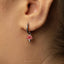 A close-up of a person's ear wearing a silver mushroom-shaped earring with a red charm.