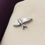 A silver pin in the shape of a bird is displayed on a beige fabric surface.