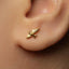 A close-up of a person's ear with a small gold earring featuring a bird design.