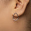 A close-up view of a person's ear wearing a silver earring with a teardrop-shaped design.