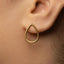 A close-up of a person's ear wearing a gold earring with a teardrop shape.