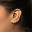 A close-up of a person's ear adorned with multiple gold earrings, including a hoop earring and a small stud.
