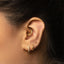 A close-up of a person's ear adorned with multiple gold earrings, including a hoop earring and two small earrings with diamonds.