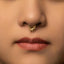 A close-up portrait of a woman with a gold nose ring and a serious expression on her face.