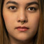 A close-up portrait of a woman with a gold nose ring and a serious expression on her face.
