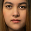 A close-up portrait of a young woman with long, dark hair and a nose piercing.