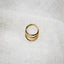 A gold hoop earring is resting on a white fabric surface.