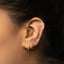 A close-up of a person's ear adorned with multiple gold earrings, including a crescent moon-shaped earring and a pair of dangling earrings.