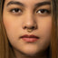 A close-up portrait of a young woman with a nose ring, looking directly at the camera with a serious expression.