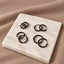 A square white marble surface displays a collection of black hoop earrings.