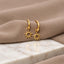 A pair of gold earrings with sun-shaped charms, resting on a white marble surface.