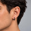 A close-up view of a person's ear with a black hoop earring.