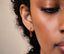 A close-up of a person's face, focusing on their ear with a small red mushroom-shaped earring.